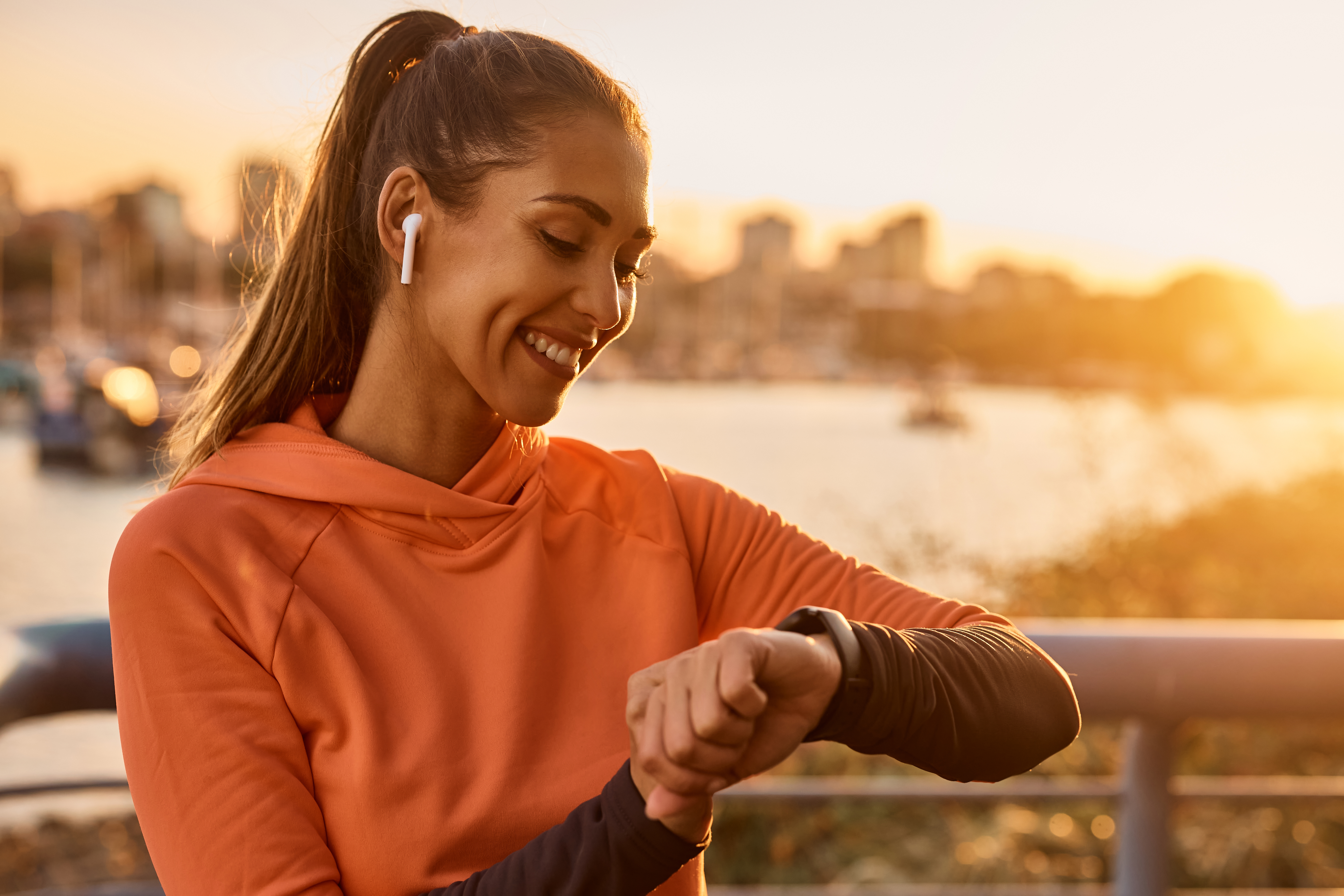Happy sportswoman using fitness tracker while exercising at sunset.